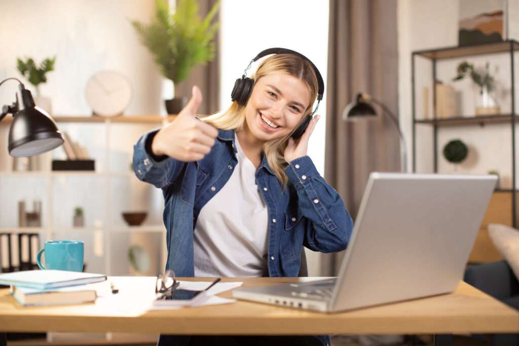 woman wearing headphones sitting table modern apartment showing victory sign gesture